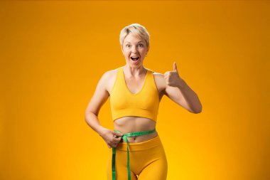 Sarı arka planda kısa saçlı, mezuralı bir kadın. Kilo kaybı ve sağlık konsepti