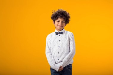 Gülümseyen mutlu çocuk 6-7 yaşlarında. Sarı arka plandaki stüdyoda