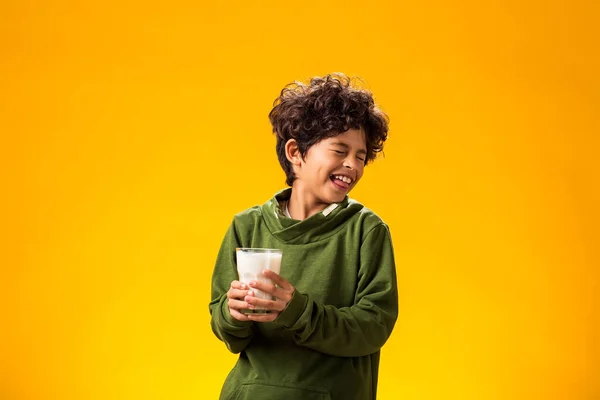 Lactose intolerance. Dairy intolerant unhappy child boy holding glass of milk over yellow background.