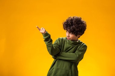 Düşünceli çocuk portresi sarı arka planda boş bir yeri işaret ediyor..