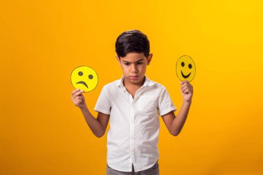 Üzgün çocuk iki parça kağıt üzerinde mutlu ve üzgün yüzler tutuyor..