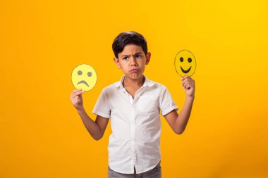 Üzgün çocuk iki parça kağıt üzerinde mutlu ve üzgün yüzler tutuyor..