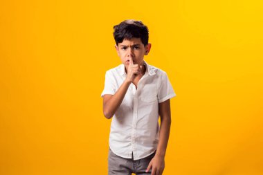 Çocuk portresi, parmaklarını dudaklarında tutuyor ve sarı arka planda sessizlik hissi veriyor..