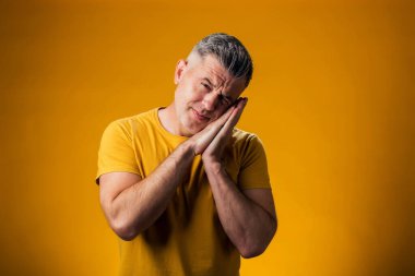 Sarı arka planda uyku jesti gösteren bir adam portresi. Rahatlama kavramı