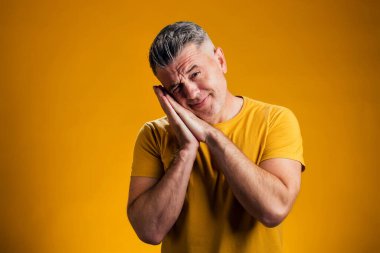 Sarı arka planda uyku jesti gösteren bir adam portresi. Rahatlama kavramı