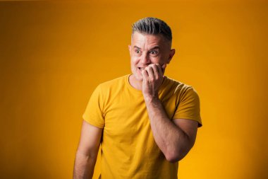 İnsan portresi gergin ve gergin, elleri ağızda, sarı arka planda tırnak yiyor. Endişe sorunu.