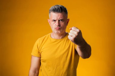 Öfkeli, öfkeli ve öfkeli bir adamın portresi sarı arka planda öfkeyle bağırırken yumruğunu kaldırıyor. Saldırgan kavram.