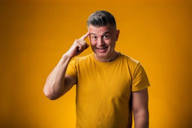 Gülümseyen adamın kafaya parmağıyla dokunuşunun portresi sarı arkaplan üzerinde harika bir fikir hareketi gösteriyor.. 