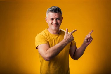 Sarı arka planda bir ürünü sergilemek için parmak gösteren bir adam portresi.