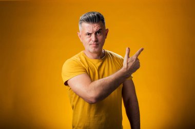 Ciddi bir adamın portresi sarı arka planda bir ürünü sergilemek için parmağıyla onu işaret ediyor.