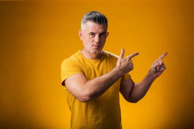 Ciddi bir adamın portresi sarı arka planda bir ürünü sergilemek için parmağıyla onu işaret ediyor.