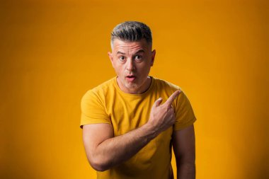 Sarı arka planda bir ürünü sergilemek için parmak gösteren bir adam portresi.