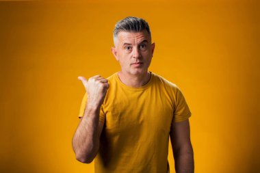 Ciddi bir adamın portresi sarı arka planda bir ürünü sergilemek için parmağıyla onu işaret ediyor.