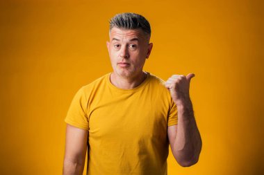 Sarı arka planda bir ürünü sergilemek için parmak gösteren bir adam portresi.