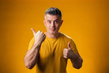 Bir ürünü sergilemek ve sarı arka planda baş parmağını gösteren bir adamın portresi.
