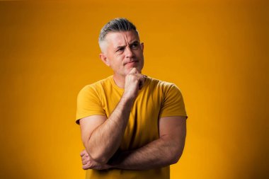 Eli çenesinde olan bir adamın portresi soru sormayı, düşünceli ifadeyi ve sarı arka planı düşünüyor. İnsanlar ve duygu kavramı