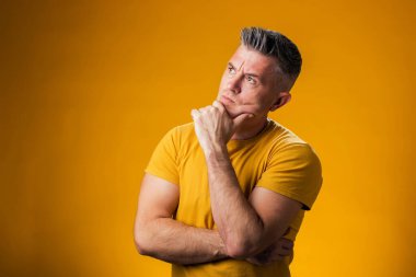 Eli çenesinde olan bir adamın portresi soru sormayı, düşünceli ifadeyi ve sarı arka planı düşünüyor. İnsanlar ve duygu kavramı