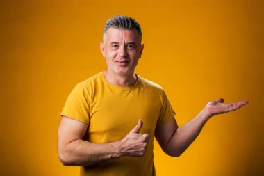 Bir ürünü sergilemek ve sarı arka planda baş parmağını gösteren bir adamın portresi.