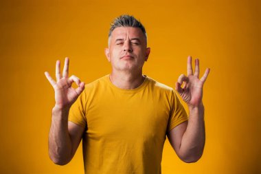 Gözleri kapalı meditasyon yapan bir adamın portresi, sakin, sarı arka planda. Rahatlama kavramı