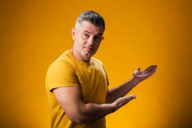 Neşeli bir şekilde gülümseyen bir adamın portresi. Avuç içiyle göstererek sarı arka plandaki kameraya bakıyor. Reklam kavramı