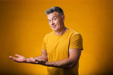 Neşeli bir şekilde gülümseyen bir adamın portresi. Avuç içiyle göstererek sarı arka plandaki kameraya bakıyor. Reklam kavramı