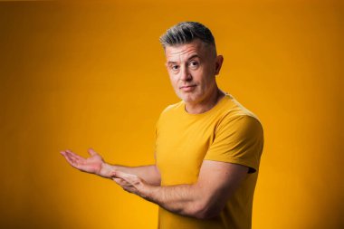 Neşeli bir şekilde gülümseyen bir adamın portresi. Avuç içiyle göstererek sarı arka plandaki kameraya bakıyor. Reklam kavramı