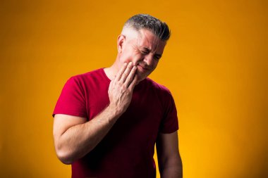 Sarı arka planda diş ağrısı çeken bir adamın portresi. Elle yanak. Halk, sağlık ve tıp konsepti