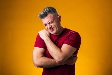 Omuz ağrısı çeken bir adamın portresi. Omuz omuza, sarı arka planda. Halk, sağlık ve tıp konsepti