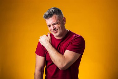 Omuz ağrısı çeken bir adamın portresi. Omuz omuza, sarı arka planda. Halk, sağlık ve tıp konsepti