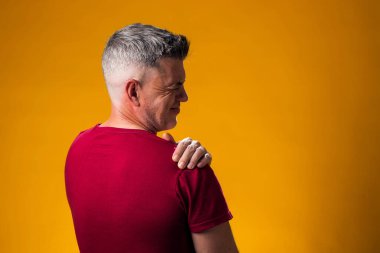 Omuz ağrısı çeken bir adamın portresi. Omuz omuza, sarı arka planda. Halk, sağlık ve tıp konsepti
