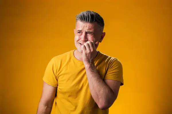 Portrait of man stressed and nervous with hands on mouth biting nails over yellow background. Anxiety problem.