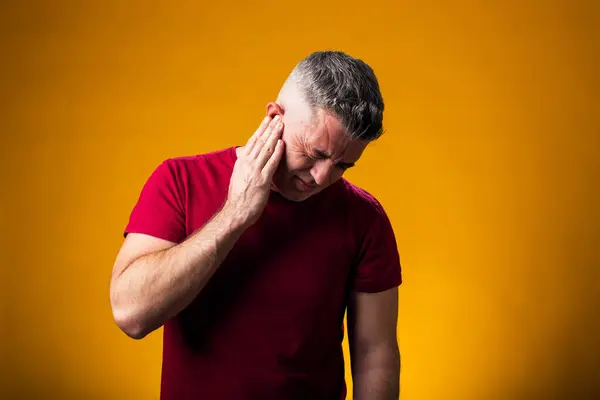 Portrait of man suffering from ear pain. Hand on ear, over yellow background. People, healthcare and medicine concept