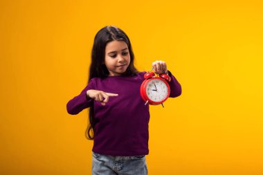 Elinde çalar saati tutan ve parmağıyla işaret eden gülümseyen kız portresi. Eğitim, okul, teslim tarihleri, öğrenim zamanı