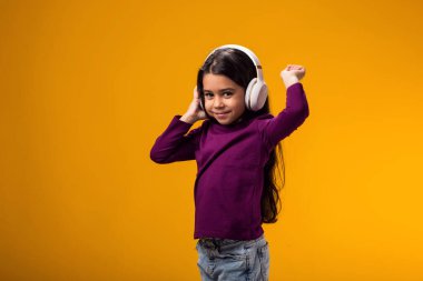 Sarı arka planda kulaklıkla müzik dinleyen pembe elbiseli gülümseyen kız portresi. Yaşam tarzı ve kiralama konsepti