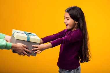 Gülümseyen kızın portresi sarı arka planda hediye kutusunu kabul ediyor. Doğum günü ve kutlama konsepti