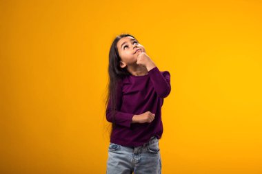 Düşünceli bir kız çocuğunun portresi parmaklarıyla çeneye dokunuyor ya da sarı arka planda düşünüyor.