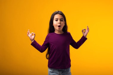 Gülümseyen kızın portresi sarı arka planda iyi bir jestle bakıyor. Pozitif duygu kavramı