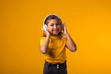 Sarı arka planda kulaklıkla müzik dinleyen pembe elbiseli gülümseyen kız portresi. Yaşam tarzı ve kiralama konsepti