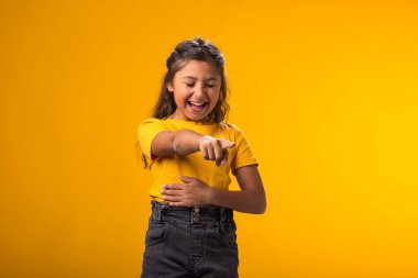 Portrait of kid girl mocking and teasing at someone showing finger at camera and holding stomach over yellow background. Bulling concept clipart