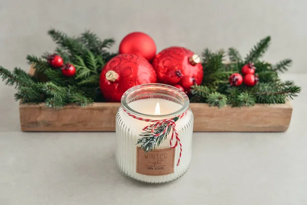 Candle in jar with christmas decorations from fir tree branches and red christmas balls on light background