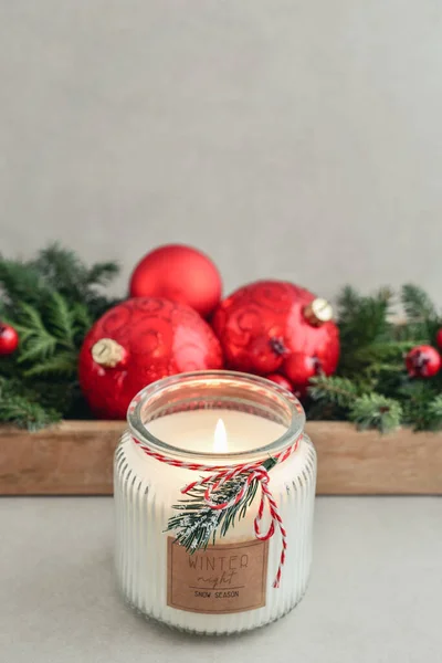 Candle in jar with christmas decorations from fir tree branches and red christmas balls on light background