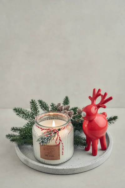 Red  ceramic deer and candle in jar with fir tree branches on stone tray on light background