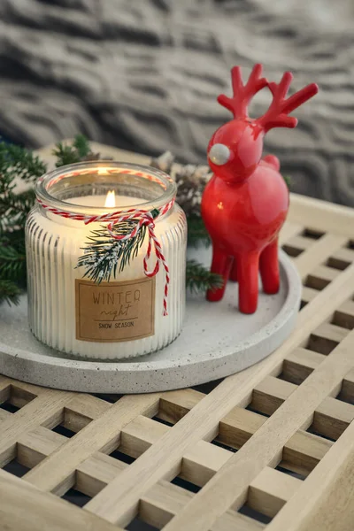 Red ceramic deer and candle in jar with fir tree branches on stone tray closeup in home interior