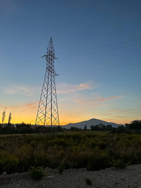 Overhead line pylons, high voltage pylons in meadow with mountains on background at summer sunset, near Oricum, Albania