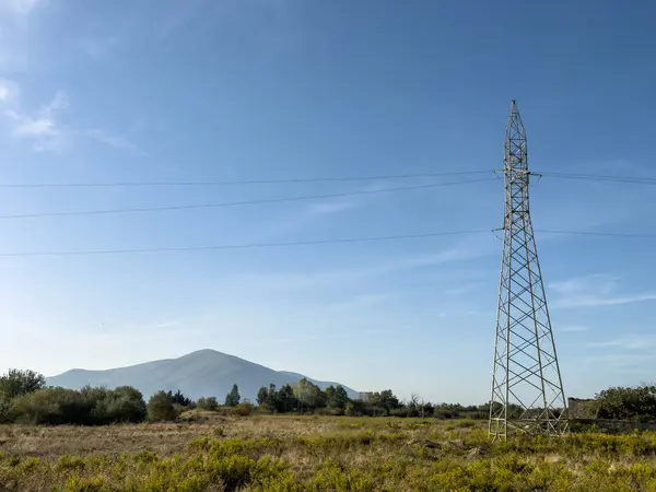 Overhead line pylons, high voltage pylons in meadow with mountains on background at summer sunny day, near Oricum, Albania