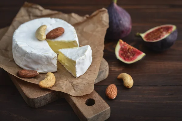 Camembert cheese with fresh figs, cashew and almond nuts served on cutting board on dark wooden background, top view