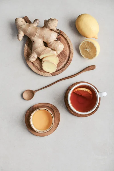 Tea  in a white cups with lemon, ginger root on cutting board and  and honey  on a light background, top view