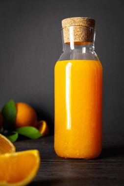 Bottle of freshly Orange juice and fresh cut orange fruits on dark wooden background, vertical composition 