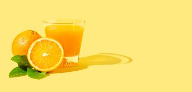 Orange juice in glass and fresh cut orange fruits on yellow background with copy space 