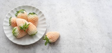 Fresh and rive white Japanese strawberries on small round plate, on light grey background 